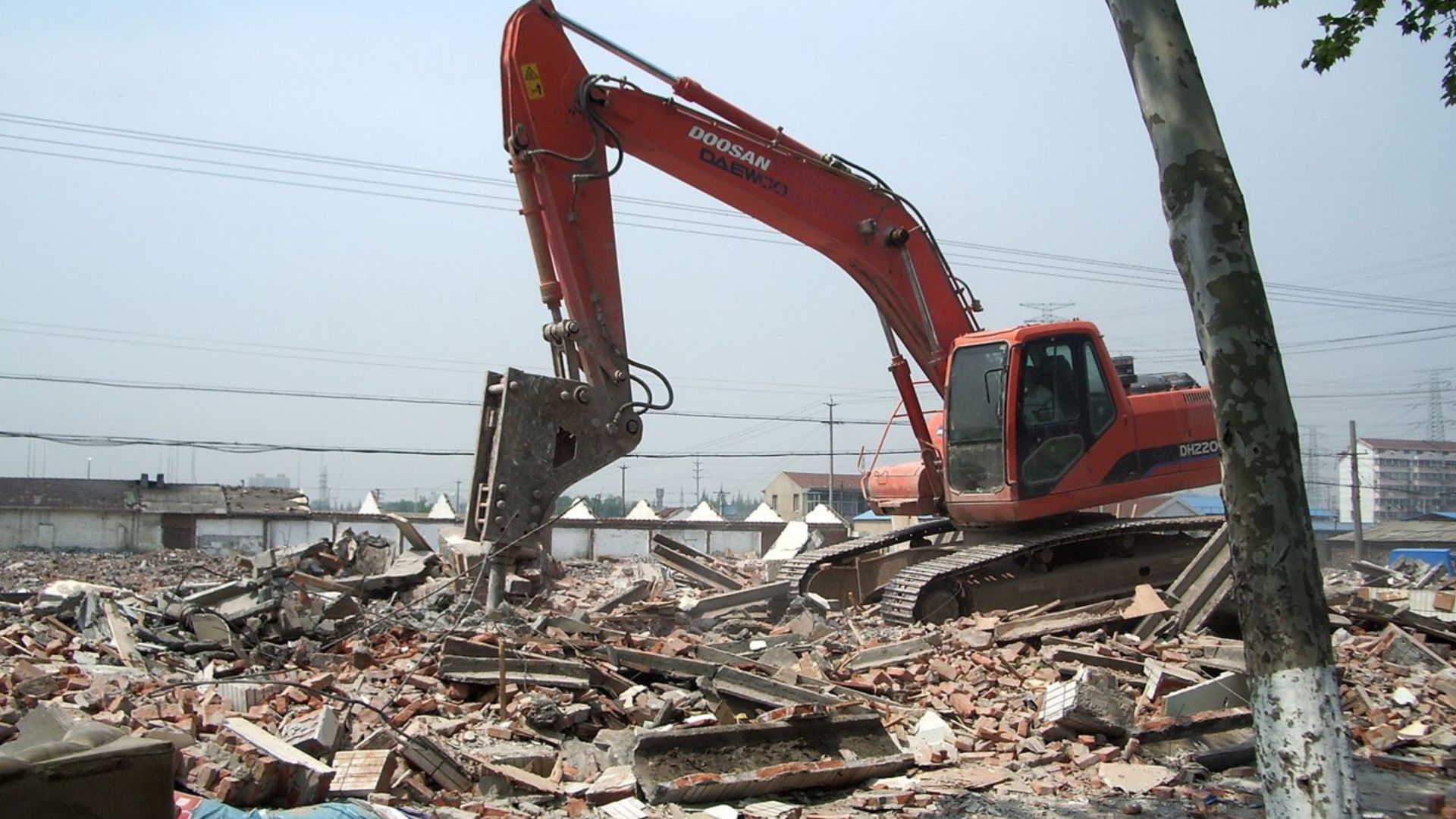 Red Doosan excavator demolishing brick buildings amid urban rubble