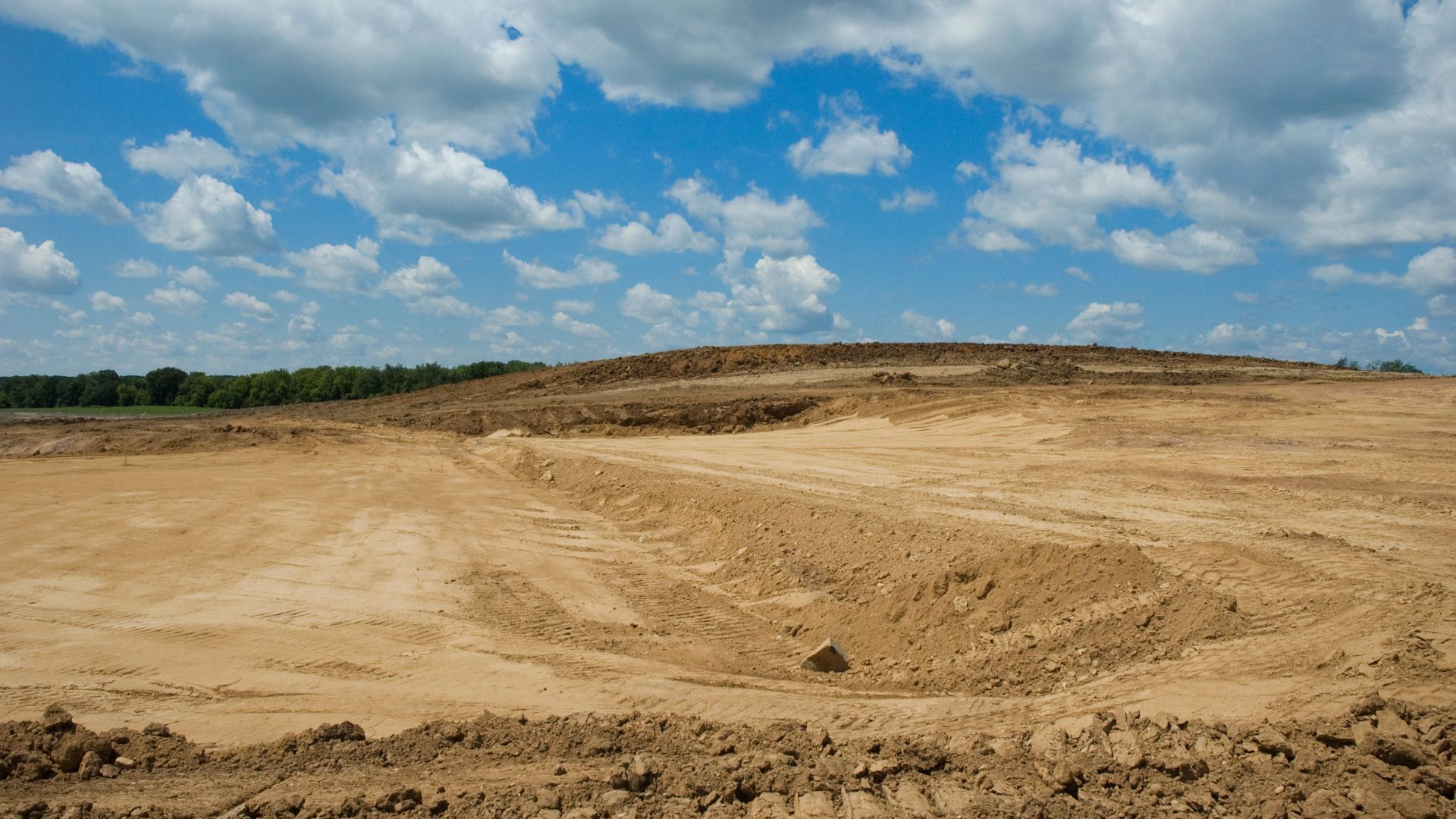 Construction site with barren earth, blue sky, and distant trees