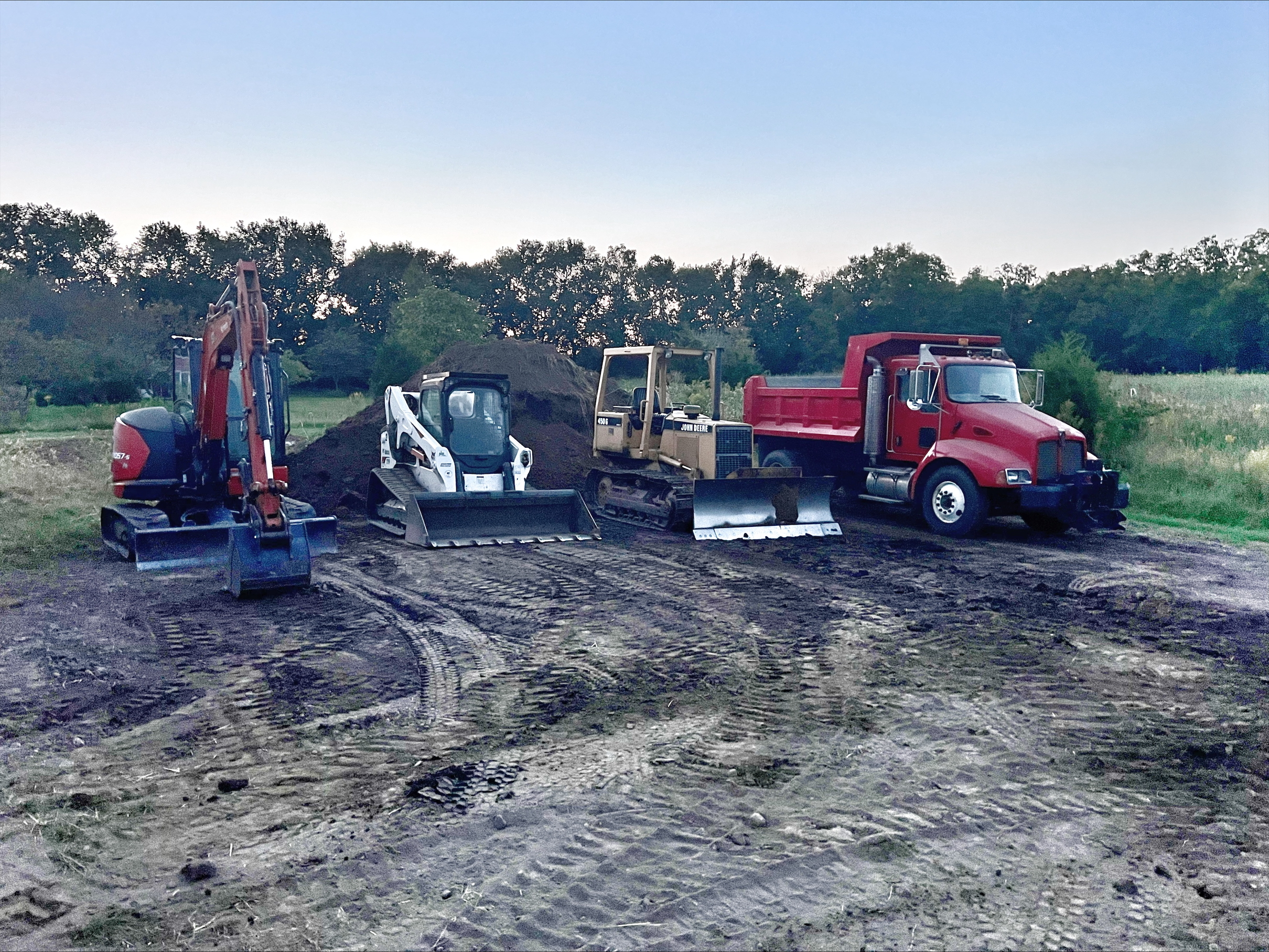 Construction site with excavator, bulldozer, skid steer, and red dump truck
